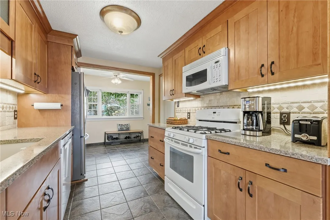 Kitchen with white appliances, tasteful backsplash, light stone countertops, a ceiling fan, and a textured ceiling