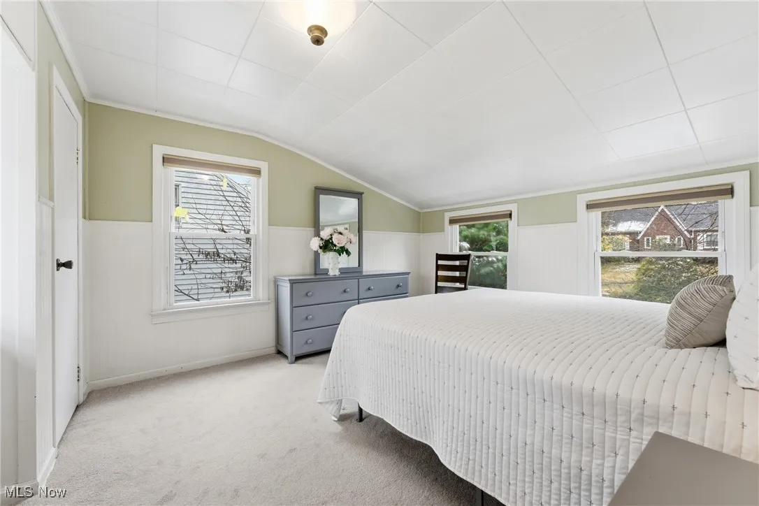 Bedroom with carpet floors, lofted ceiling, multiple windows, and a wainscoted wall