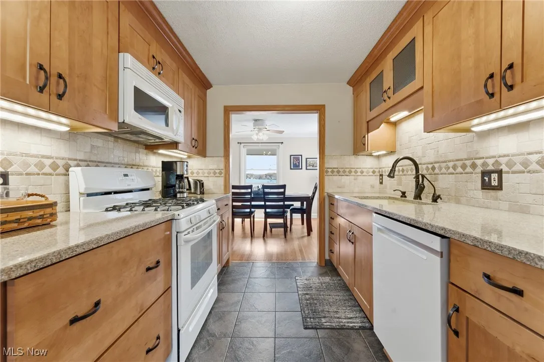 Kitchen featuring white appliances, light stone countertops, ceiling fan, decorative backsplash, and glass insert cabinets