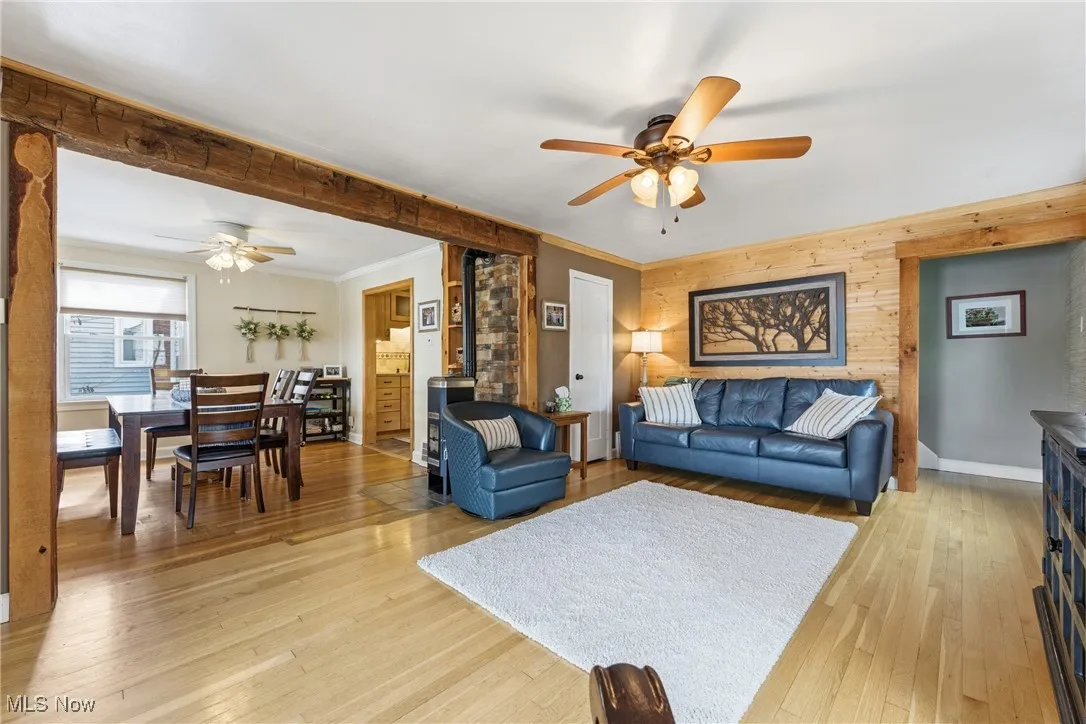 Living area with ceiling fan, crown molding, light wood finished floors, and wood walls