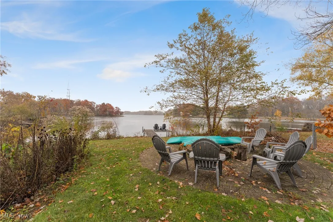 View of green lawn with a fire pit, a patio, and a water view