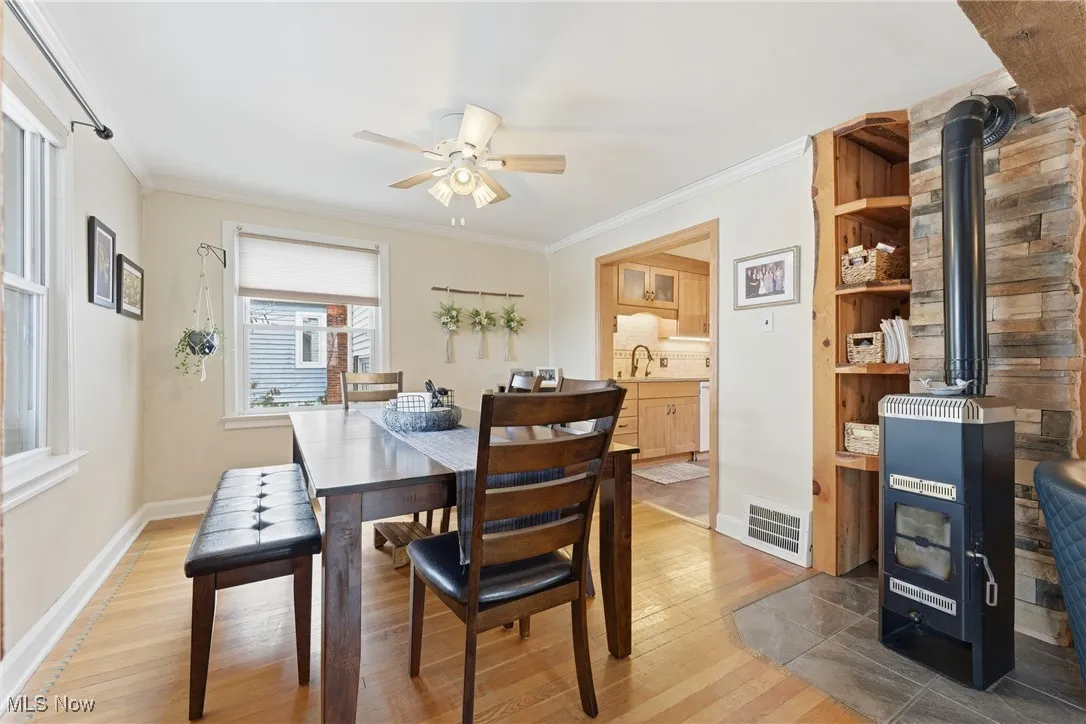 Dining area featuring a wood stove, light wood-style flooring, ornamental molding, and ceiling fan