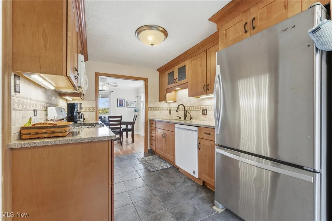 Kitchen with white appliances, light stone countertops, glass insert cabinets, decorative backsplash, and brown cabinetry