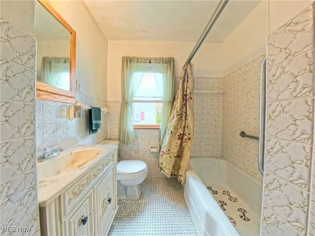 Full bathroom with vanity, shower / bathtub combination with curtain, tile walls, light tile patterned floors, and wainscoting