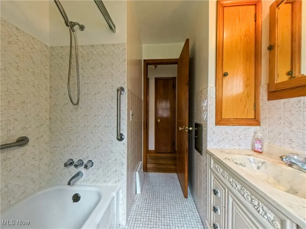 Full bathroom featuring vanity, bathtub / shower combination, tile walls, and light tile patterned flooring