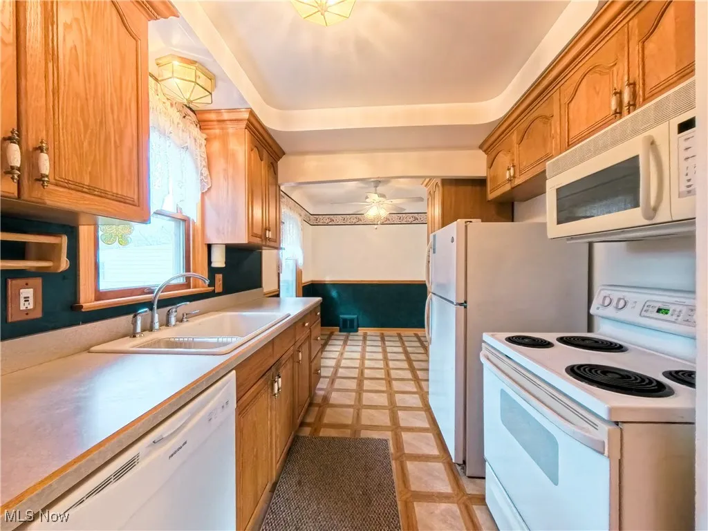Kitchen with white appliances, a wainscoted wall, light countertops, brown cabinets, and ceiling fan