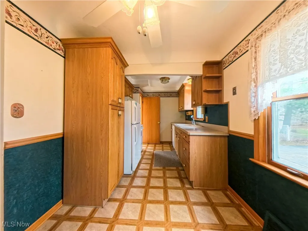 Kitchen with wainscoting, brown cabinetry, light countertops, inlaid floor details, and open shelves
