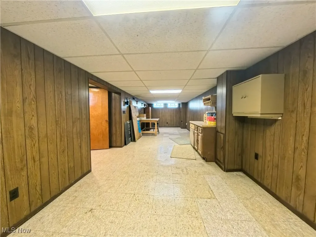 Basement featuring light flooring, wood walls, and a drop ceiling