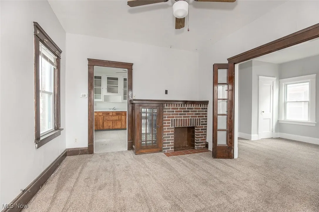 Unfurnished living room with light carpet, healthy amount of natural light, a brick fireplace, and ceiling fan