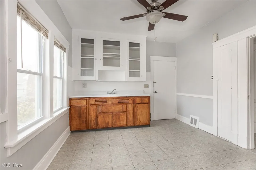 Bar area with light countertops, glass insert cabinets, brown cabinetry, and a ceiling fan