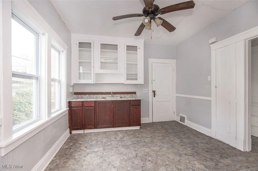 Bar with glass insert cabinets, decorative backsplash, a ceiling fan, white cabinetry, and dark brown cabinetry