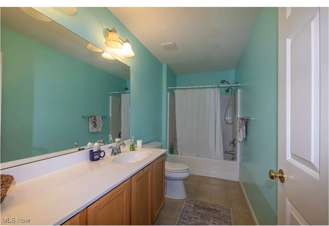 Full bathroom with vanity, shower / bath combination with curtain, and dark tile patterned flooring