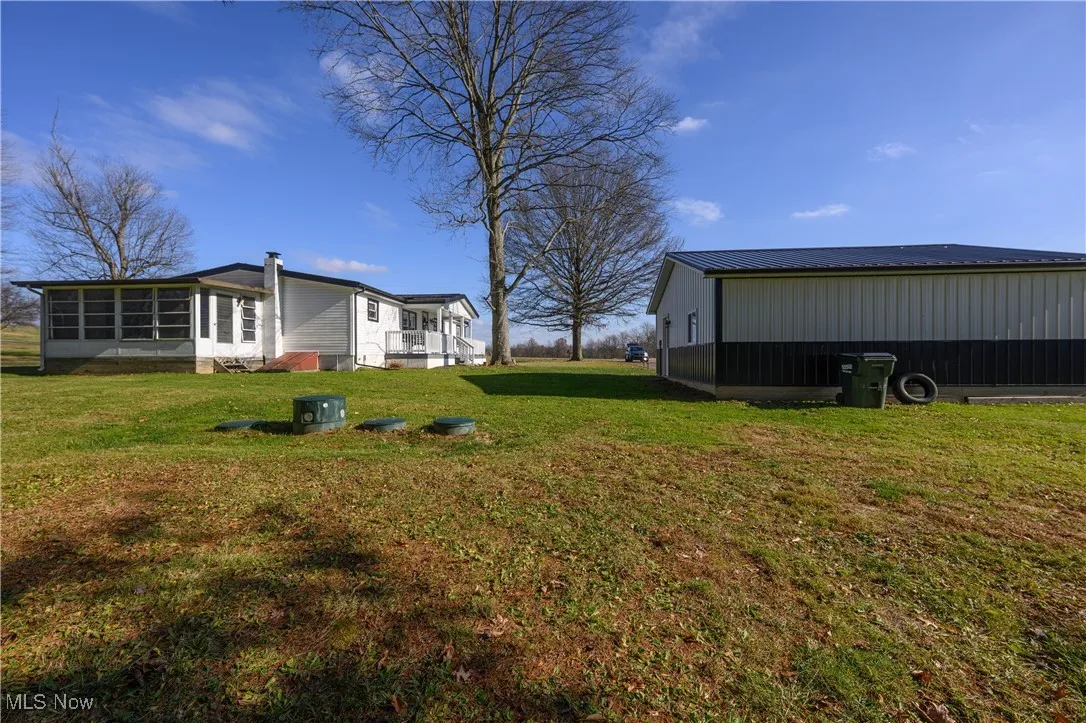 View of grassy yard featuring an outbuilding, a pole building, and a sunroom