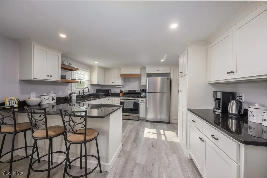 Kitchen featuring open shelves, appliances with stainless steel finishes, a peninsula, white cabinets, and light wood finished floors