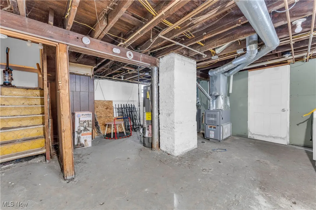 Unfinished basement with heating unit, stairs, and gas water heater