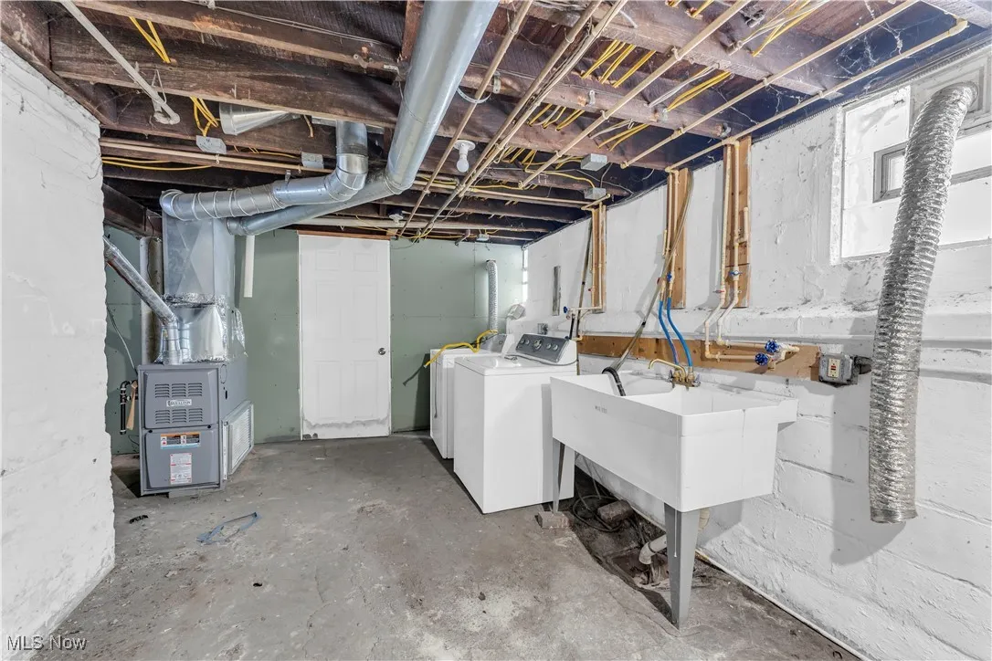 Unfinished below grade area featuring heating unit and washing machine and clothes dryer