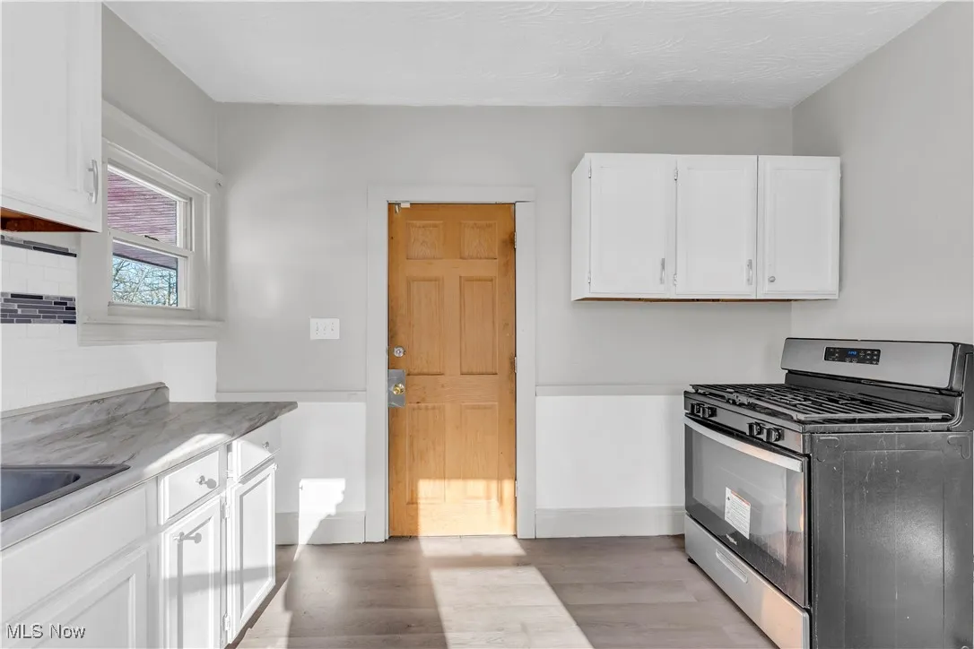 Kitchen with stainless steel range with gas cooktop, white cabinets, light wood finished floors, tasteful backsplash, and light countertops