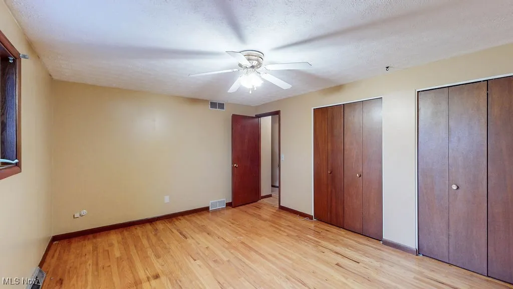 Unfurnished bedroom with two closets, light wood-style flooring, a ceiling fan, and a textured ceiling