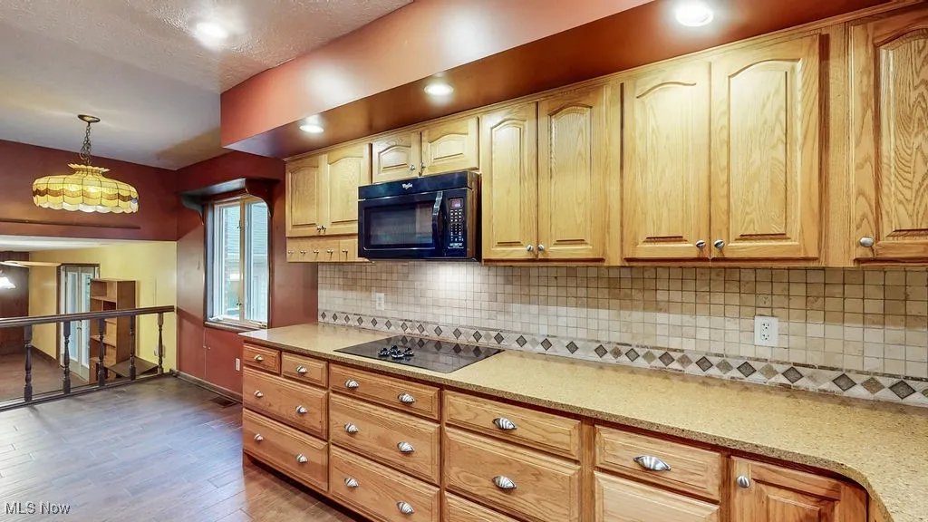 Kitchen with black appliances, decorative backsplash, decorative light fixtures, light wood-style flooring, and light stone countertops