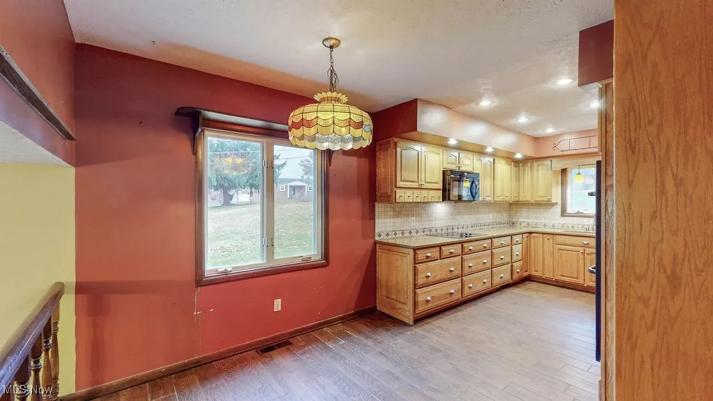 Kitchen with light countertops, light wood-style flooring, backsplash, pendant lighting, and black microwave
