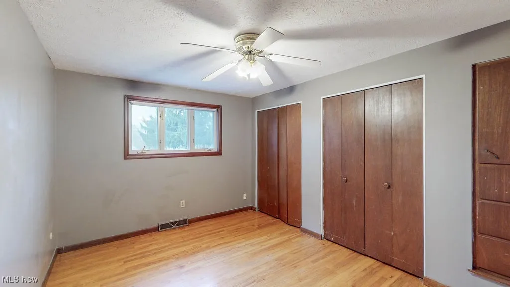 Unfurnished bedroom with multiple closets, light wood finished floors, ceiling fan, and a textured ceiling