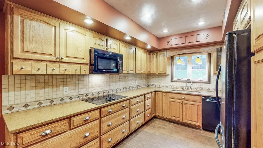 Kitchen with black appliances, decorative backsplash, light wood-style flooring, and recessed lighting