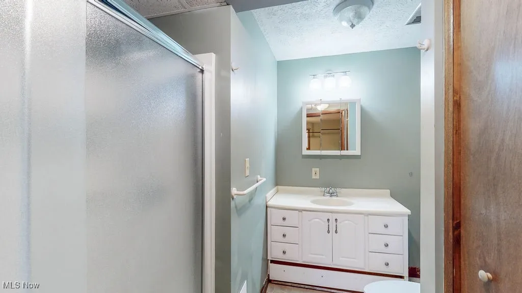 Full bath with vanity, a stall shower, and a textured ceiling