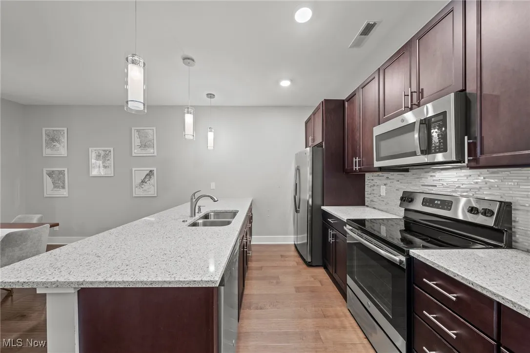 Kitchen with stainless steel appliances, dark brown cabinets, light wood-type flooring, light stone counters, and recessed lighting