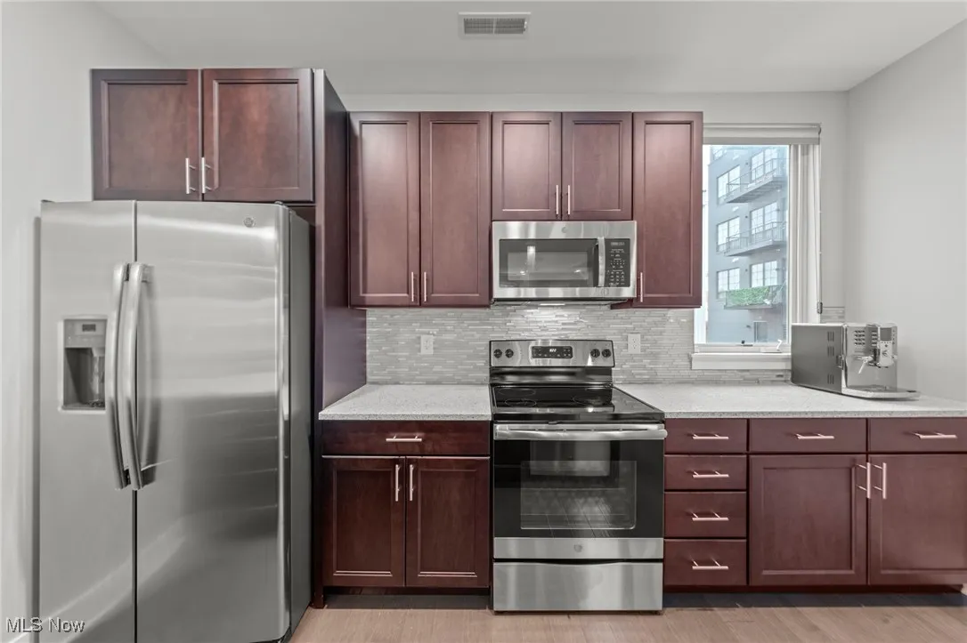 Kitchen with appliances with stainless steel finishes, backsplash, light stone countertops, and light wood-style flooring
