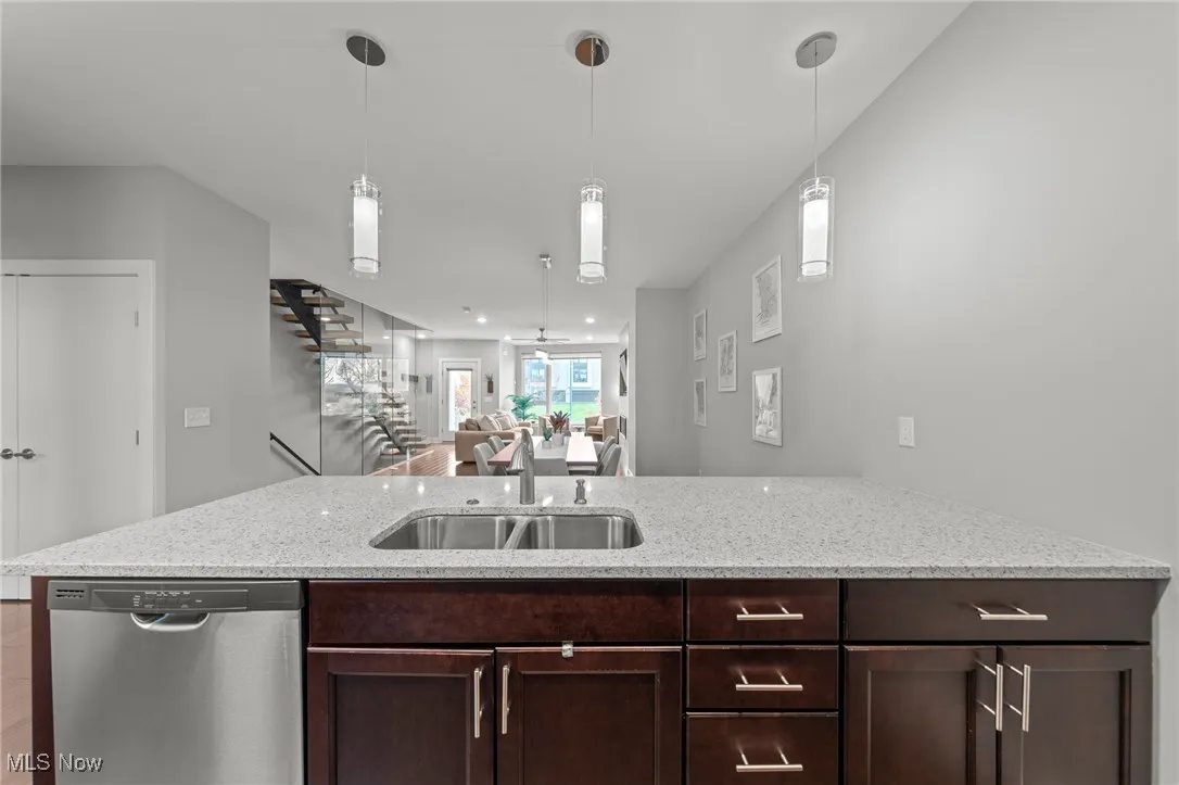 Kitchen with dishwasher, dark brown cabinetry, light stone countertops, and open floor plan