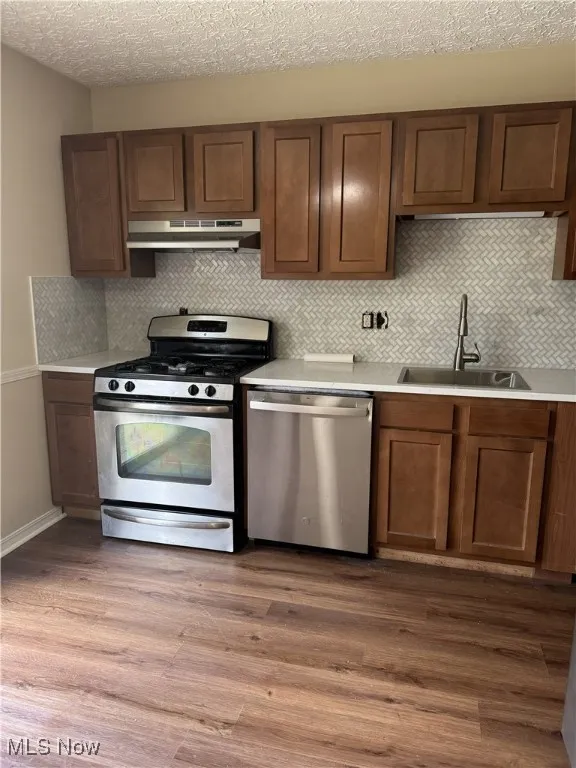 Kitchen featuring appliances with stainless steel finishes, tasteful backsplash, dark wood finished floors, a textured ceiling, and under cabinet range hood