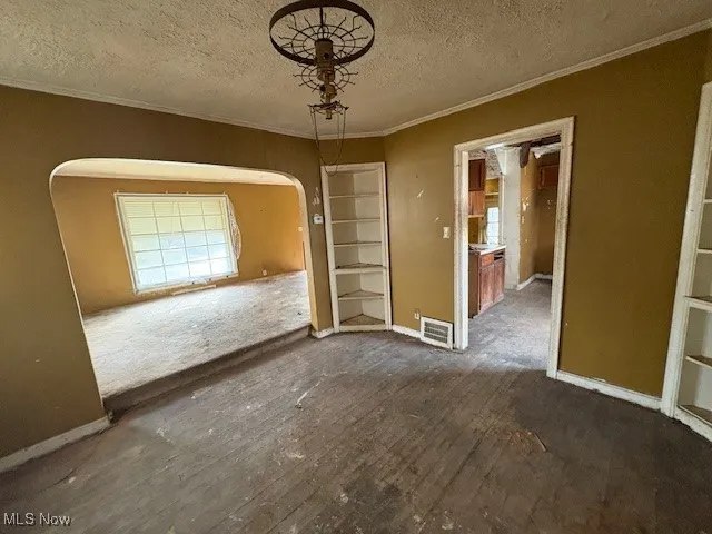 Unfurnished dining area with ornamental molding, built in shelves, a textured ceiling, and arched walkways