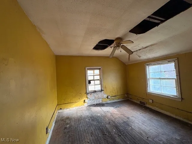 Spare room with a textured ceiling, vaulted ceiling, ceiling fan, and hardwood / wood-style flooring