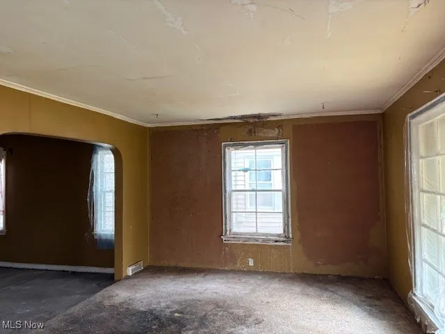 Empty room with healthy amount of natural light, arched walkways, and ornamental molding