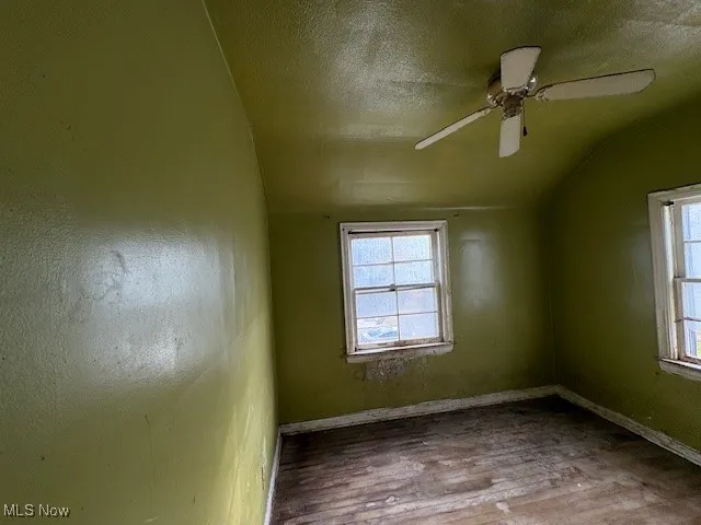 Empty room with a textured ceiling, lofted ceiling, wood finished floors, and a ceiling fan