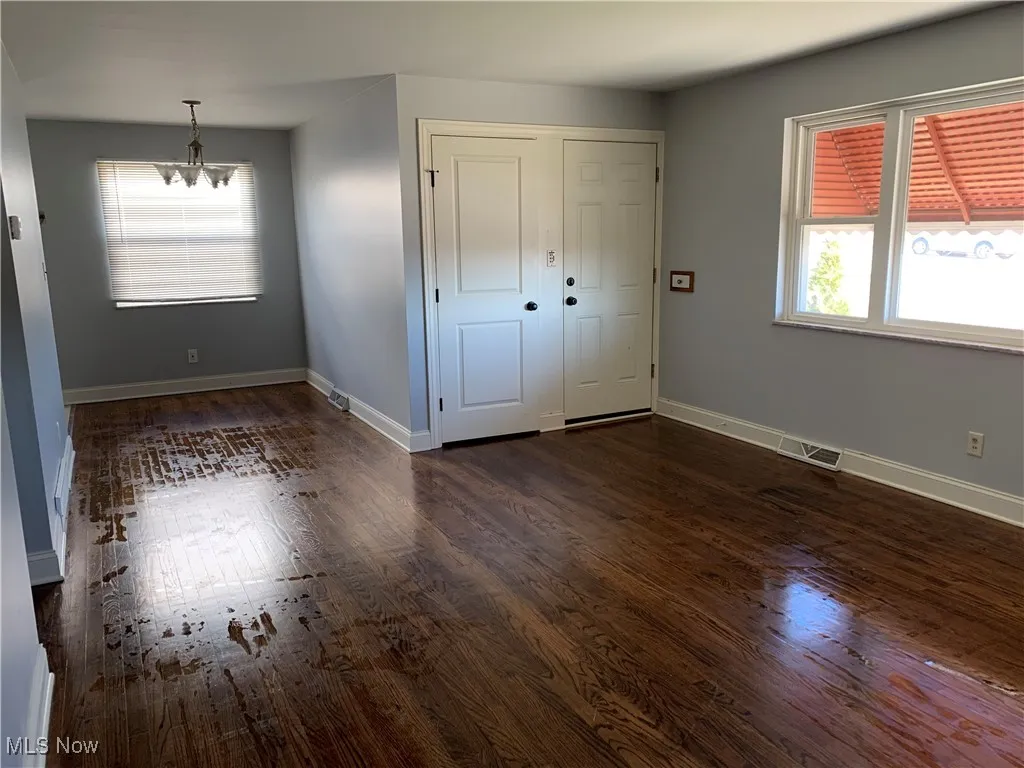 Unfurnished bedroom with dark wood-style floors, multiple windows, and a chandelier