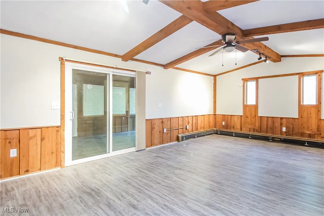 Spare room with wood finished floors, a wainscoted wall, wooden walls, ceiling fan, and baseboard heating