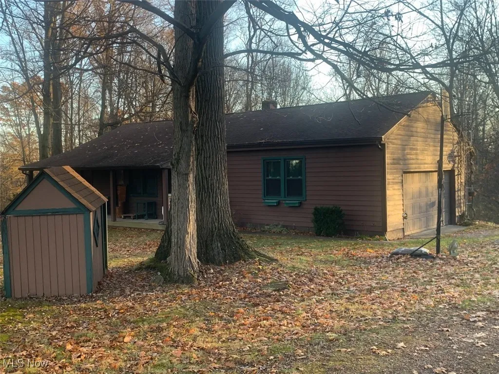 View of side of property featuring a storage shed, a chimney, and a shingled roof