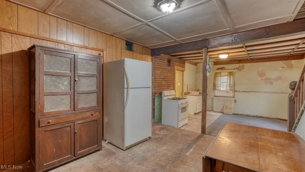 Kitchen with white appliances, wooden walls, brown cabinets, brick wall, and concrete floors