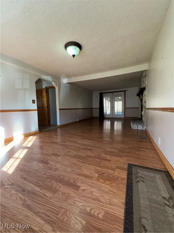 Unfurnished living room featuring light wood finished floors, a textured ceiling, arched walkways, and french doors