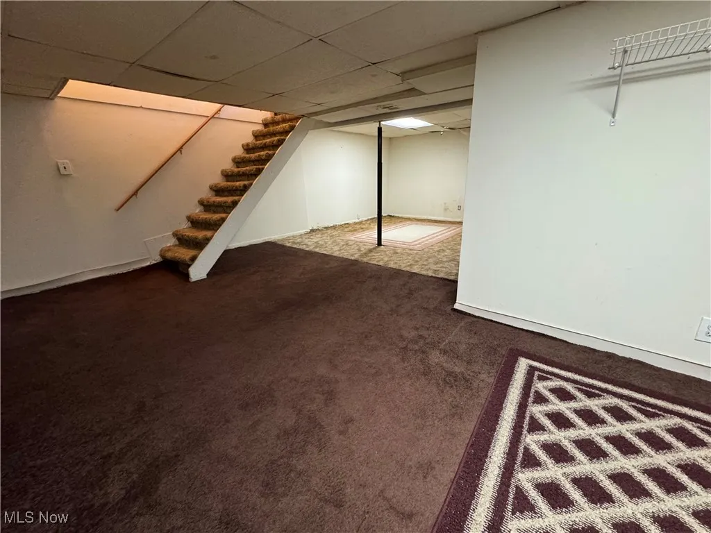 Finished below grade area featuring a drop ceiling, stairway, and dark carpet