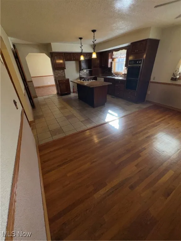 Kitchen featuring a textured ceiling, pendant lighting, a kitchen island, dark wood-type flooring, and double wall oven