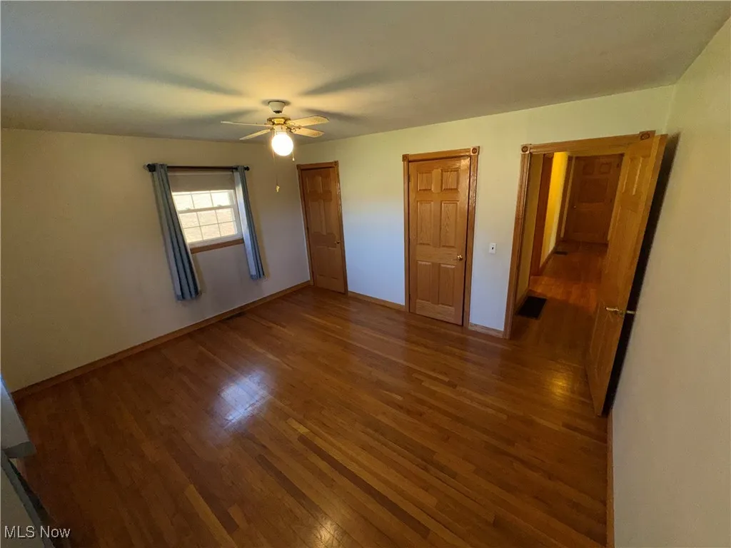 Unfurnished bedroom with two closets, dark wood-type flooring, and ceiling fan