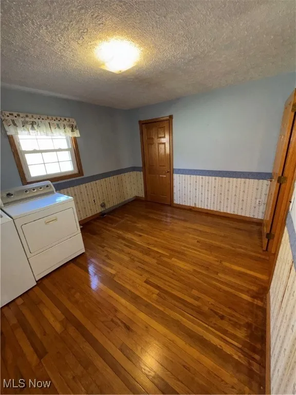 Laundry room featuring dark wood finished floors, a textured ceiling, wallpapered walls, and wainscoting