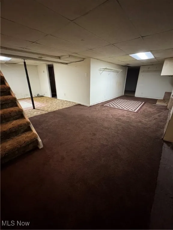 Finished basement with a paneled ceiling, carpet, and stairway
