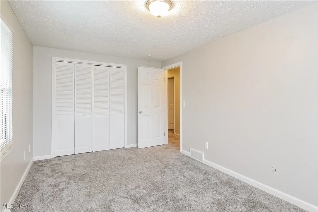 Unfurnished bedroom featuring a textured ceiling, carpet flooring, a closet, and multiple windows