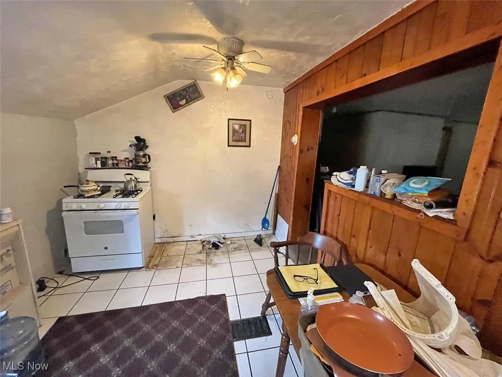 Kitchen featuring light tile patterned flooring, white gas range oven, wood walls, vaulted ceiling, and a ceiling fan