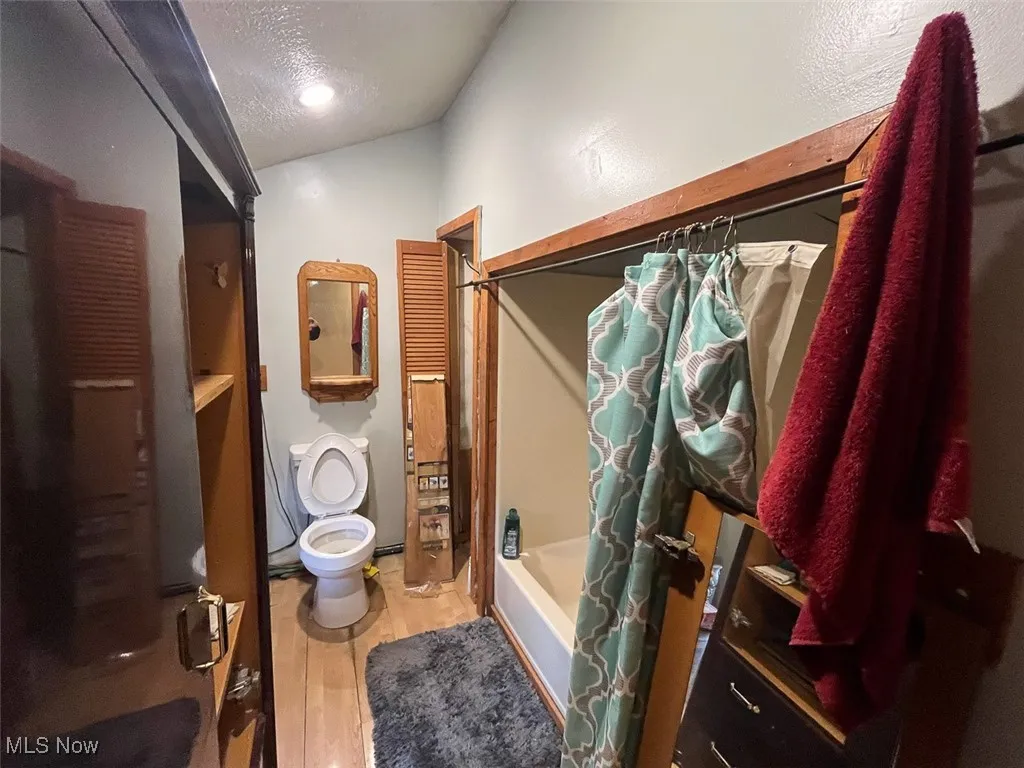 Full bathroom with a textured ceiling, shower / tub combo, and light wood-style floors