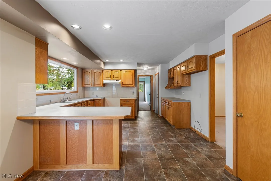 Kitchen featuring a peninsula, backsplash, light countertops, brown cabinets, and recessed lighting