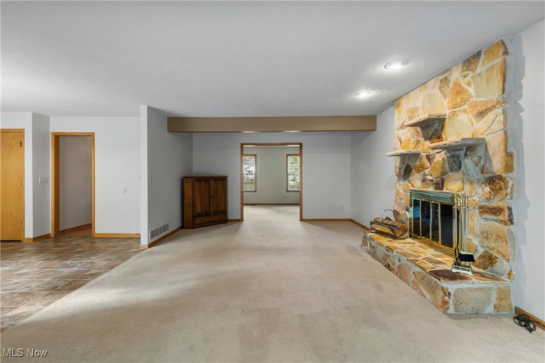 Unfurnished living room featuring a stone fireplace, carpet, and stone finish floors